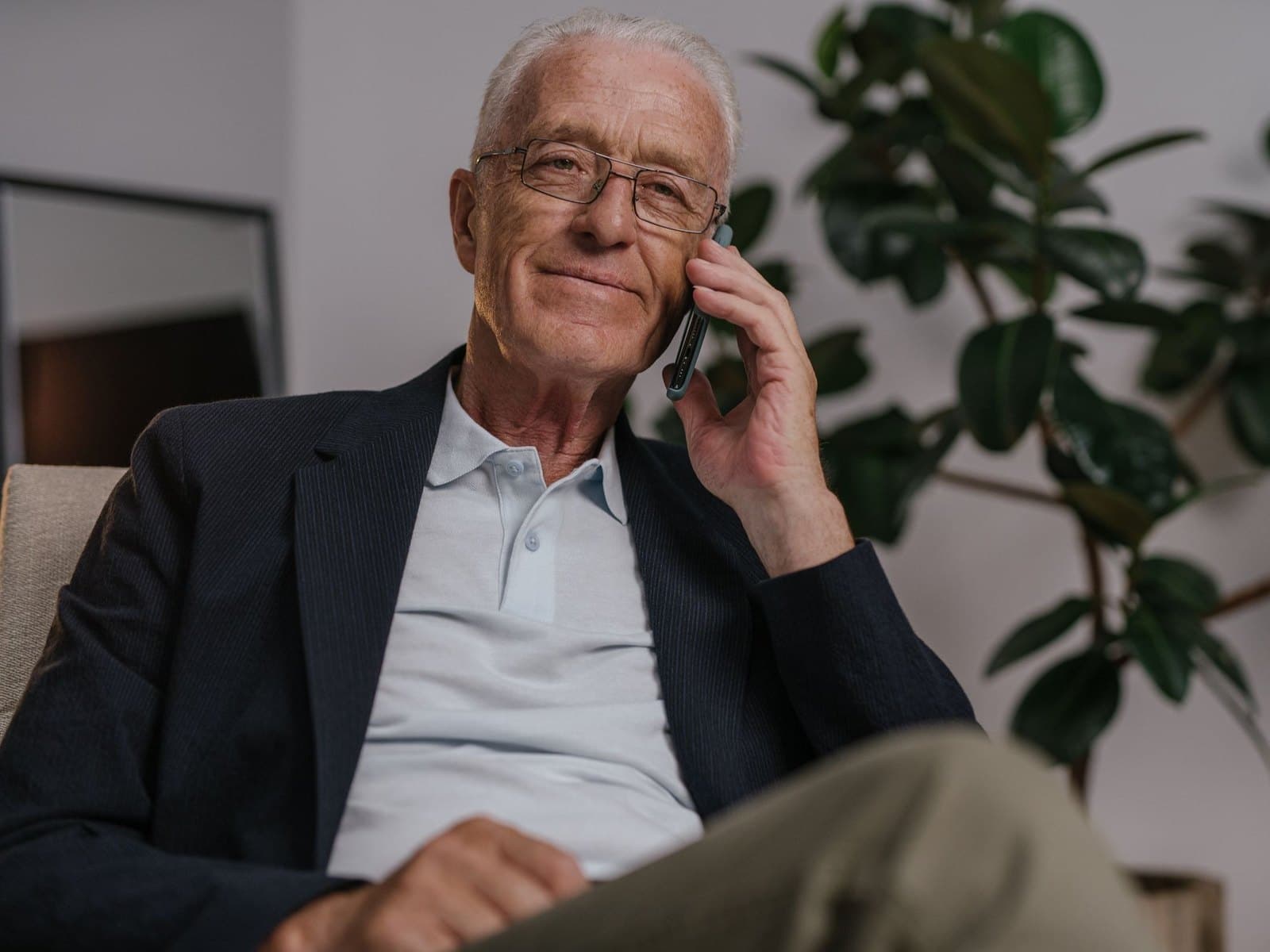 An older man smiling as he talks on the phone at home
